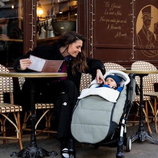 Bébé dans une chancelière grise installée sur une poussette en terrasse